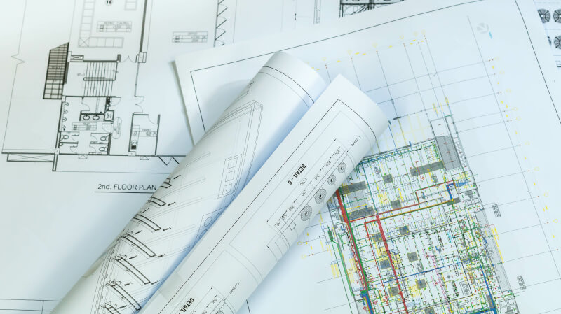 Rozłożone i zwinięte plany architektoniczne z widocznymi rzutami pięter oraz szczegółowymi schematami technicznymi.